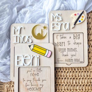 May include: Three wooden teacher appreciation plaques with personalised messages and decorative elements. The top plaque says "Ms. Esra" with a paint palette and paintbrush. The middle plaque says "Mr. Iyos" with a crescent moon and a mosque. The bottom plaque says "Eleni" with a pencil and says "Just a little note to say thank you for being my teacher."