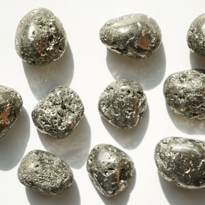 May include: A collection of ten smooth, metallic, gray-toned pyrite stones. The stones are various sizes and shapes, and have a rough, textured surface.