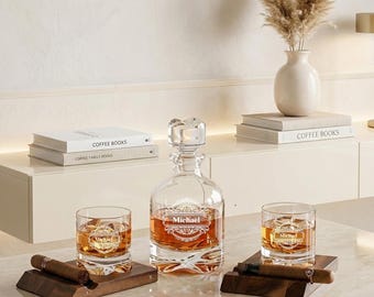 May include: A clear glass decanter and two matching whiskey glasses, each engraved with the name Michael in a decorative frame. The set includes two dark wood cigar rests, each holding a brown cigar, arranged on a polished marble surface.
