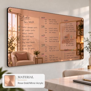 May include: A rectangular rose gold mirror acrylic dry erase board featuring a weekly planner layout with the text Studio This Week, days of the week, a task checklist, notes, ideas, and goals. The board is mounted with four gold-toned hardware studs.