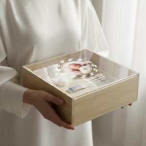 Könnte beinhalten: Holz-Andenkenbox mit transparentem Acryl-Deckel. Im Inneren befinden sich weiße Babysocken, ein Krankenhausarmband und ein Foto eines Neugeborenen. Der Deckel zeigt ein kreisförmiges Design mit Babyfüßen und dem Namen des Babys, Isabella.