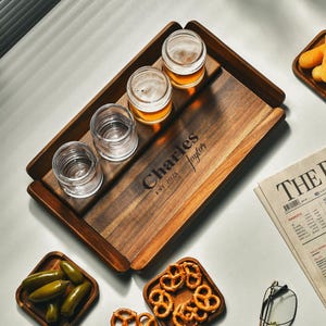 May include: A wooden beer flight set with four small glasses, two filled with beer. The wooden tray has the name "Charles Taylor" and "EST 2025" engraved on it. The set is surrounded by small dishes of snacks.