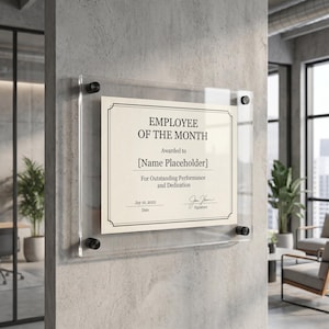 May include: A clear acrylic frame displays an "Employee of the Month" certificate on a concrete wall. The certificate has a cream-colored background with black text and a decorative border. The text includes "Awarded to [Name Placeholder]" and "For Outstanding Performance and Dedication."