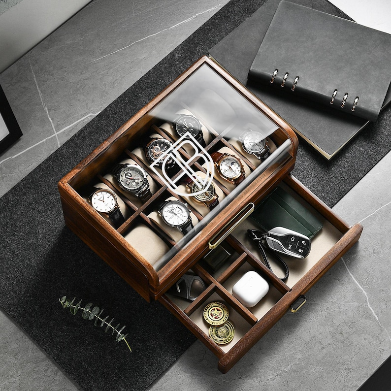 Puede incluir: Una caja de madera para relojes con tapa de cristal, que muestra varios relojes de pulsera. El caj&oacute;n contiene accesorios como una cartera, llaves del coche y monedas. Los relojes tienen diferentes colores de correa y dise&ntilde;os de esfera.