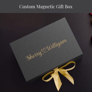 A gray gift box with a gold ribbon tied around it, placed on a dark surface.