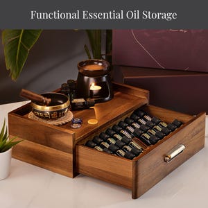 May include: A wooden essential oil storage box with a drawer filled with small bottles. The top level holds a candle-lit oil diffuser, a singing bowl, and other essential oil bottles. The text "Functional Essential Oil Storage" is at the top.