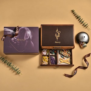 May include: A dark wooden storage box with a gold Om symbol and the name Sherry printed on the lid. The box features a pull-out drawer containing incense cones, crystals, dried herbs, and orange slices. A purple gift box and a metal incense holder.