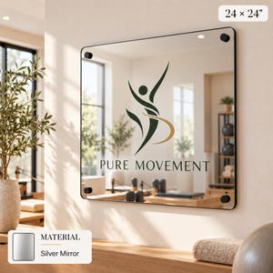 a silver mirror with the logo of Pure Movement displayed on it. The mirror is mounted on a wall and is surrounded by various decorative elements, such as a potted plant and a vase.