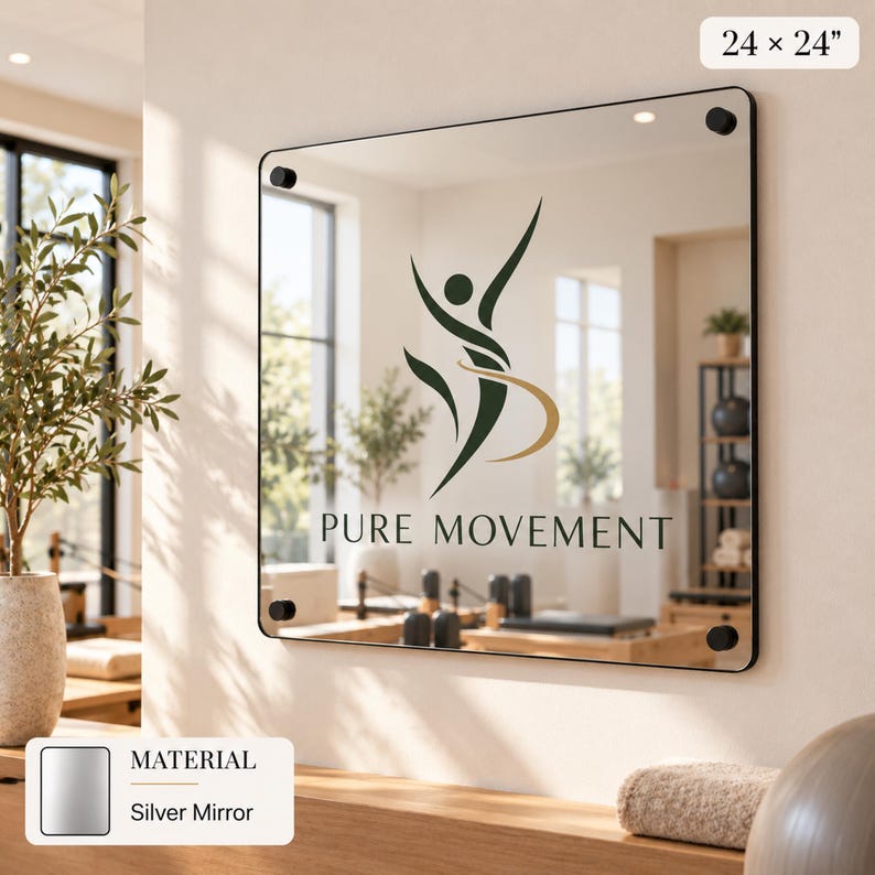 a silver mirror with the logo of Pure Movement displayed on it. The mirror is mounted on a wall and is surrounded by various decorative elements, such as a potted plant and a vase.