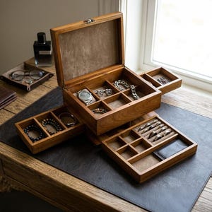 May include: A wooden jewelry organizer box with a hinged lid and multiple pull-out compartments. The interior is lined with tan fabric and contains various accessories including a silver wristwatch, metal chains, beaded bracelets, and several rings.