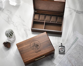 May include: A dark wood watch box with a hinged lid featuring a compass rose engraving and the name Taylor. The interior includes five cushioned watch slots and two open compartments lined with brown fabric, plus a gold-tone metal latch.