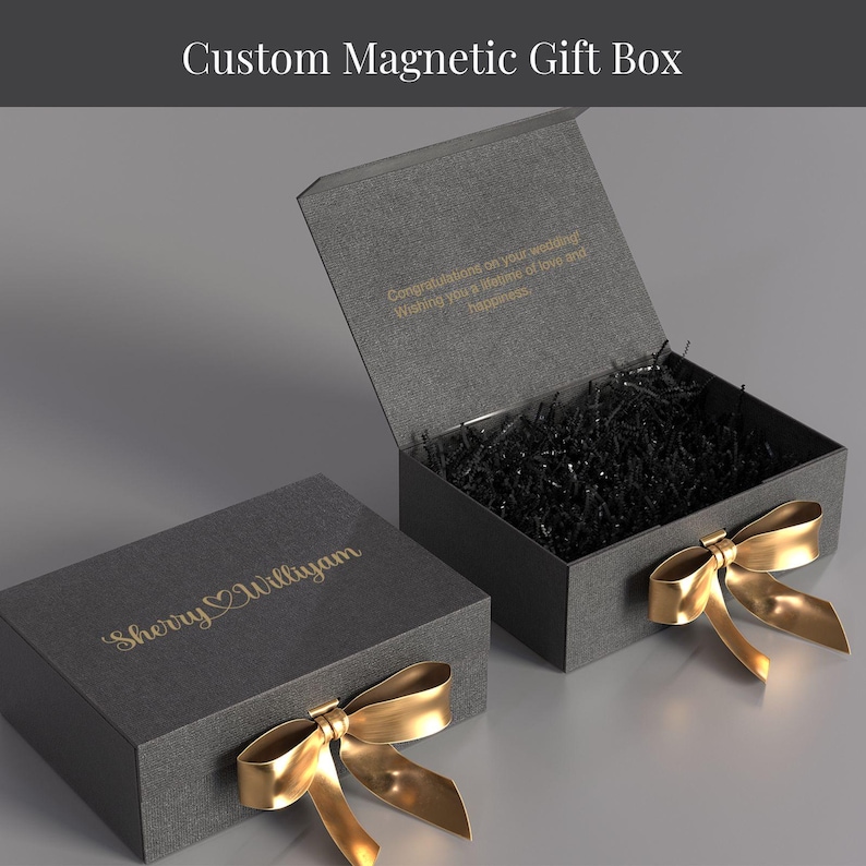 two gray gift boxes with gold bows, one open and the other closed, both placed on a gray surface.
