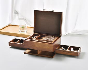 May include: A dark brown wooden jewelry box with an open lid and two side-extending drawers. The interior features multiple compartments for organizing rings, necklaces, and small accessories, with a dark brown lining throughout.