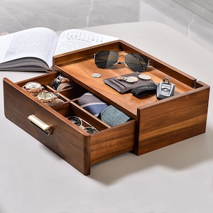 May include: A wooden valet tray with a pull-out drawer featuring a gold-toned handle. The top surface holds sunglasses, a wallet, coins, and a car key fob. The open drawer contains two wristwatches on cushions and two folded neckties.
