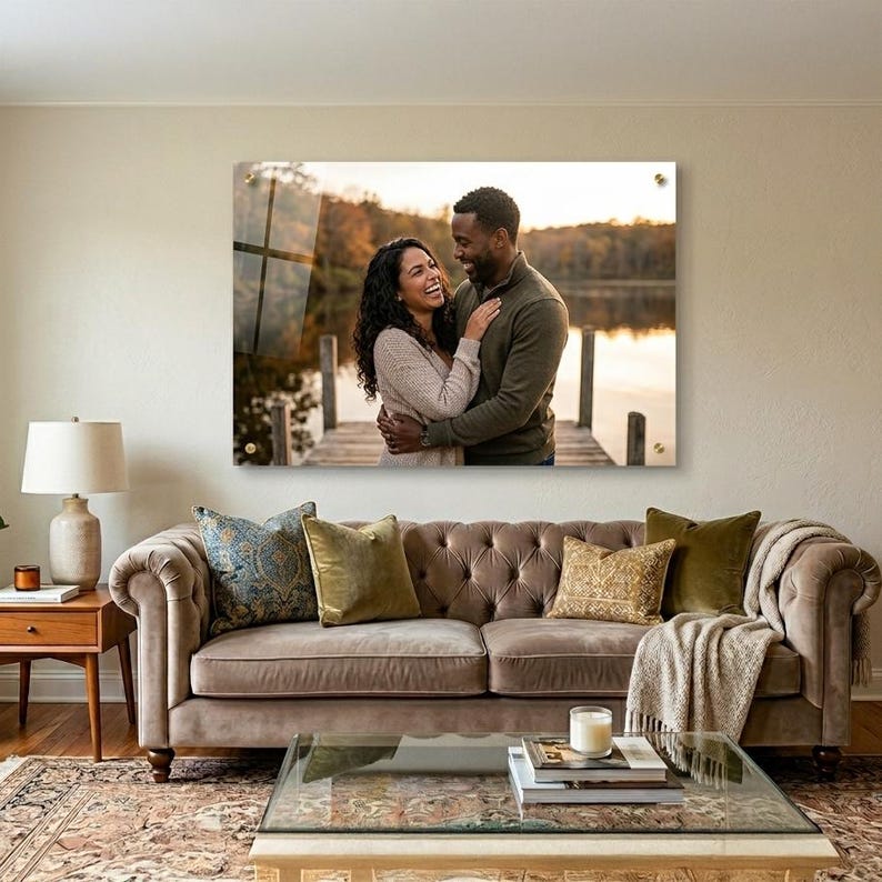 Puede incluir: Una gran impresi&oacute;n acr&iacute;lica rectangular de una pareja abraz&aacute;ndose en un muelle, exhibida sobre un sof&aacute; marr&oacute;n con cojines decorativos. La impresi&oacute;n est&aacute; montada en una pared beige, con una l&aacute;mpara y una mesa auxiliar a la izquierda.