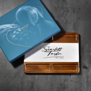 May include: A rectangular wooden serving board with a central white marble inlay featuring the black printed text Scarlett Taylor and EST. 6.14.1975. The board includes four recessed compartments and is paired with a blue box labeled SHANIK.