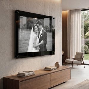 May include: A rectangular wall-mounted acrylic photo frame featuring a black border and silver mounting hardware. The frame displays a black and white photograph of a couple in wedding attire, with the person on the left wearing a veil.