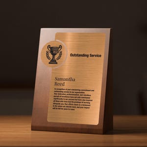May include: A wooden plaque with a gold-colored plate. The plaque reads "Outstanding Service" and includes the name "Samantha Reed." A trophy graphic is at the top left. The plaque has a brown wooden base.