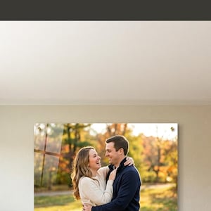 Puede incluir: Una impresi&oacute;n acr&iacute;lica de una pareja abraz&aacute;ndose, exhibida en una pared sobre un sof&aacute;. La imagen es parte de una escena de decoraci&oacute;n del hogar, con el texto "What to do with wedding photos after event" y "SHOP NOW". La direcci&oacute;n del sitio web tambi&eacute;n es visible.