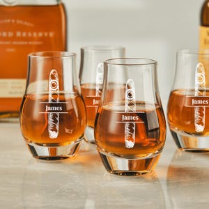several glasses filled with a golden liquid, likely whiskey, and each glass has a personalized name engraved on it.
