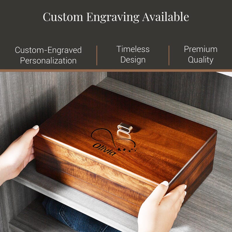 A person's hands are holding a wooden box with a custom engraving on it, which features the name "Olivia" and a heart symbol. The box is described as having custom engraving available, suggesting it is a personalized item.