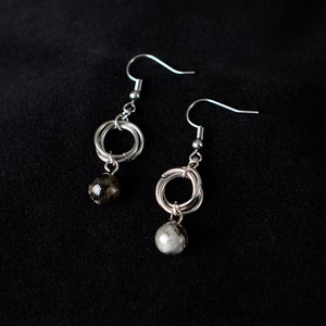 May include: A pair of silver earrings with a circle design and a black and white bead dangling from each earring.