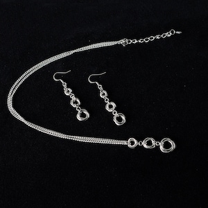 May include: A silver necklace and matching earrings with a chain link design and multiple interconnected circles. The necklace has a lobster clasp closure.