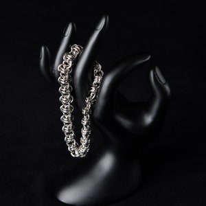 Puede incluir: Un brazalete de cadena de plata con un diseño entrelazado único, exhibido en una mano de maniquí negra.