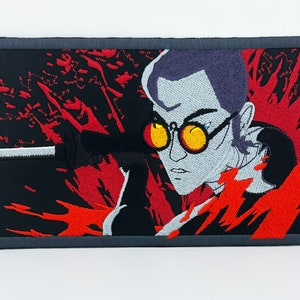 May include: Embroidered patch featuring a stylized illustration of a man with dark hair and yellow glasses, holding a gun. The background is a red and black abstract design.