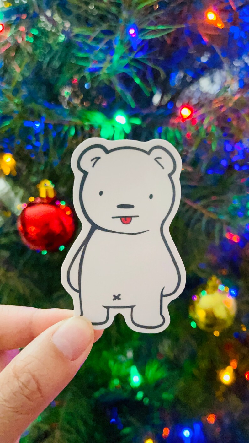 May include: A white polar bear sticker with a black outline and a red tongue sticking out. The sticker is on a blurry background of a Christmas tree with colorful lights.
