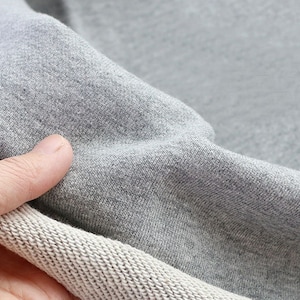 May include: Close-up of a gray sweatshirt fabric with a white ribbed trim. The fabric is soft and textured.