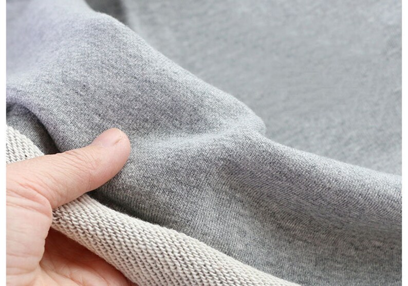May include: Close-up of a gray sweatshirt fabric with a white ribbed trim. The fabric is soft and textured.