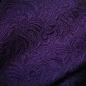 May include: Purple fabric with a raised floral pattern. The fabric has a textured, almost quilted look.