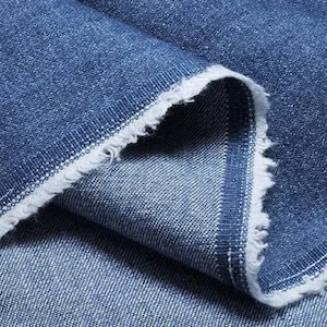 May include: Close-up of a blue denim fabric with a raw edge. The fabric is folded over itself, showing the texture and weave of the material.