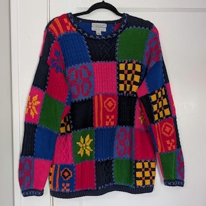 May include: A patchwork sweater in a variety of colors, including blue, pink, green, and yellow. The sweater features a crew neck and long sleeves. The design includes geometric and floral patterns.