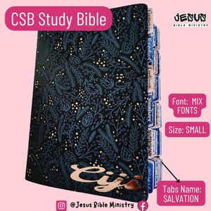 May include: A small CSB Study Bible with a black cover featuring a botanical pattern of blue and gold leaves and pinecones. The book includes index tabs labeled with book names like Genesis and Exodus, and the word Eiji in gold script.