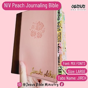 May include: A pink NIV Peach Journaling Bible with a floral embossed design on the cover. The spine has colorful tabs with the names of the books of the Bible. The cover is personalized with the name "Jamaika Adkins". The text "JESUS BIBLE MINISTRY" is visible on the cover.