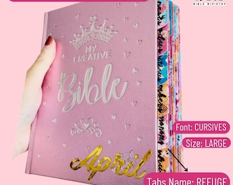Può includere: Una Bibbia rosa ESV da colorare e scrivere con le parole "My Creative Bible" in scrittura argentata. La parola "April" è in scrittura dorata. Le schede sono etichettate "Refuge". La Bibbia è grande e ha un carattere corsivo.