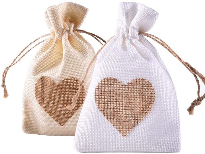 May include: Two small burlap drawstring bags with a heart-shaped design. The bags are made of natural burlap fabric and have a light brown color. The hearts are made of a darker brown burlap fabric.