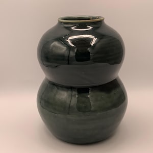 May include: A dark green ceramic vase with a rounded, hourglass shape. The vase has a glossy finish.