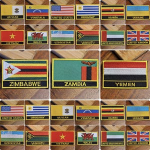 May include: A collection of embroidered patches featuring flags from various countries, including the United States, United Kingdom, Vietnam, Uruguay, and Zimbabwe. The patches are arranged in a grid pattern on a wooden surface.