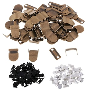 May include: A collection of metal hook and eye closures in various colors. The image shows a pile of antique bronze closures, along with smaller piles of black and silver closures. The closures are used for garments and other sewing projects.
