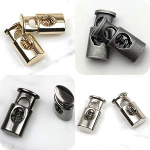 May include: A collection of metal cord locks in gold, antique silver, gunmetal, and silver finishes. Each cord lock features a spring mechanism and a decorative design on the front. These are ideal for various crafting and apparel projects.