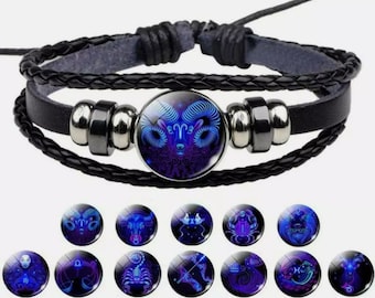 Può includere: Un braccialetto in pelle nera con un ciondolo di vetro che presenta un simbolo zodiacale blu. Il ciondolo è circondato da perline argentate. Il braccialetto è intrecciato e presenta un design intrecciato. L'immagine mostra anche 12 diversi simboli zodiacali.