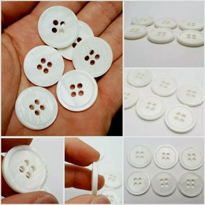 May include: A collection of white, round, four-hole buttons. The buttons are made of a pearlescent material and have a smooth, polished finish.