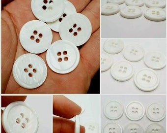 May include: A collection of white, round, four-hole buttons. The buttons are made of a pearlescent material and have a smooth, polished finish.