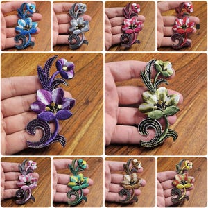 Könnte beinhalten: Sortiment von zehn gestickten Bügeletiketten mit einem floralen Design mit drei Blüten und Blättern. Die Etiketten sind in verschiedenen Farben erhältlich, darunter Blau, Grün, Lila, Rot und Gelb.