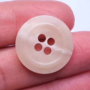 Peut inclure: Un bouton blanc à quatre trous avec une surface lisse légèrement texturée.