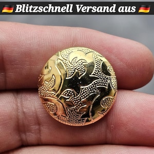 Könnte beinhalten: Ein goldfarbener, runder Knopf mit geprägtem floralem Design. Der Knopf hat ein glänzendes Finish und wird in der Hand einer Person gehalten. Der Text "Blitzschnell Versand aus" steht oben.