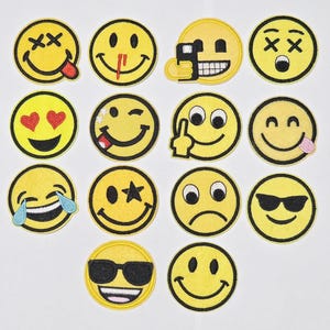 Op de afbeelding: Een verzameling gele, geborduurde patches met verschillende emoji-gezichten. Elke patch heeft een zwarte omtrek en toont verschillende uitdrukkingen, waaronder glimlachen, knipogen en het dragen van een zonnebril. Sommige emoji's hebben extra details zoals harten, tranen of een uitgestoken tong.